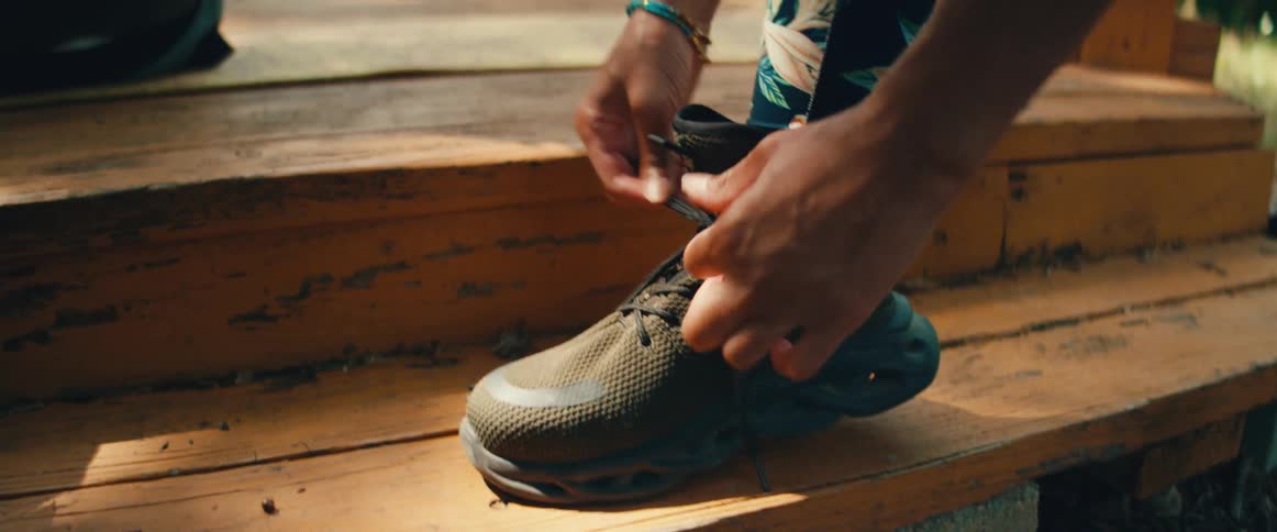 A close-up of a person in floral leggings tying the laces on their athletic shoes on a wooden step outdoors
