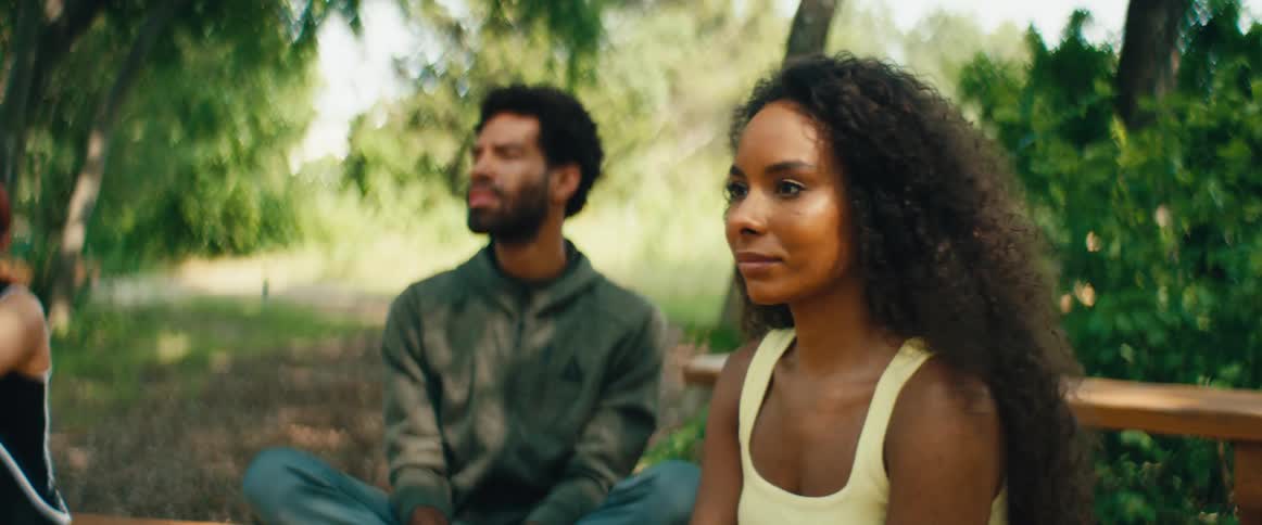 A calm African American man explains breathing techniques to a woman as they practice mindfulness together in a tranquil park