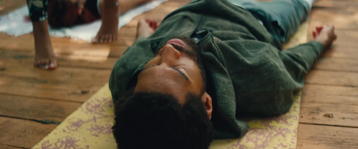 A tranquil man with eyes closed lies on a yoga mat in Savasana, finding peace during an outdoor meditation session