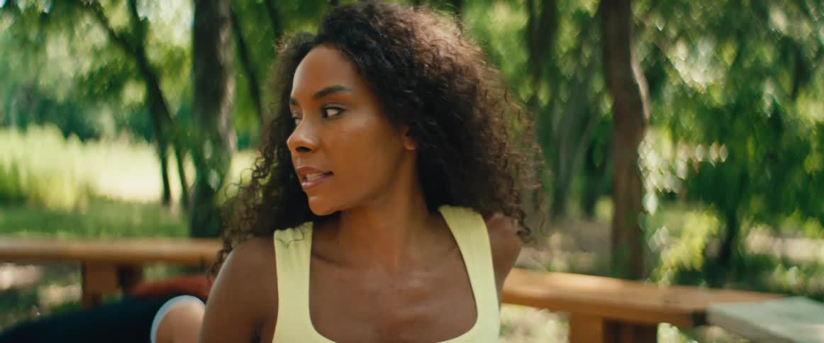 A beautiful Black woman with curly hair gracefully stretches and practices yoga in a serene, sun-dappled park in slow motion