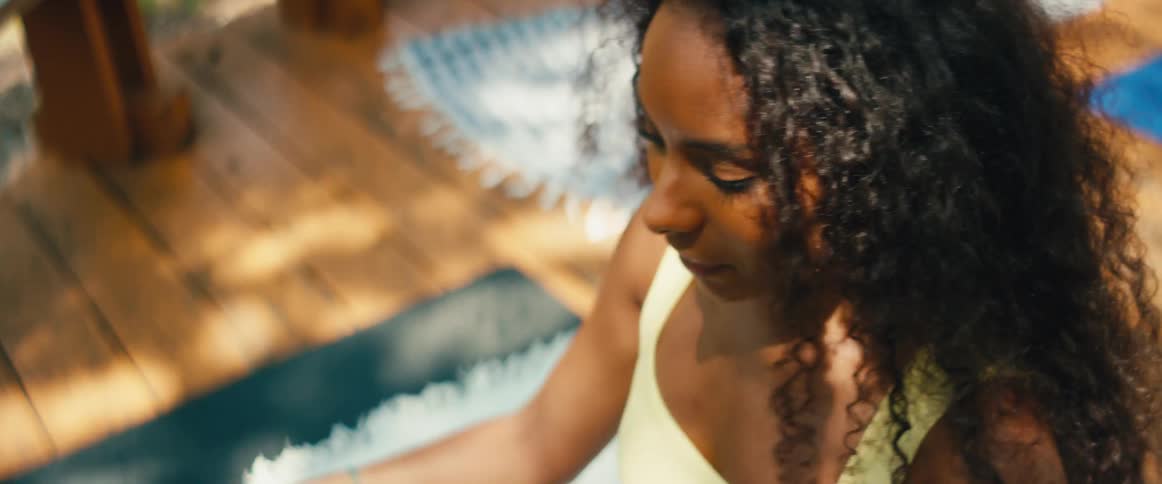 A woman with curly hair finds a moment of peace while stretching her legs during an outdoor yoga session on a sunny deck