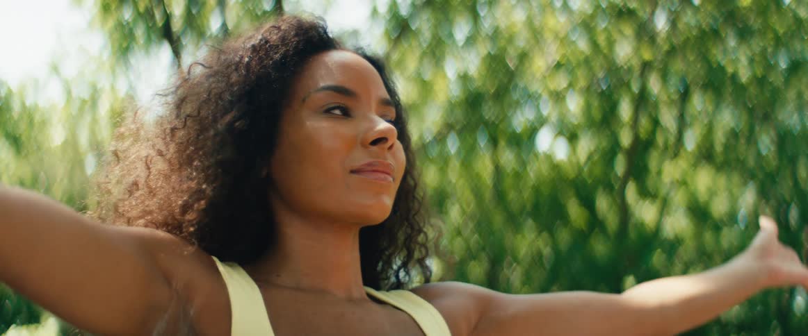 A serene woman with curly hair practices yoga and mindfulness in a lush, green outdoor setting