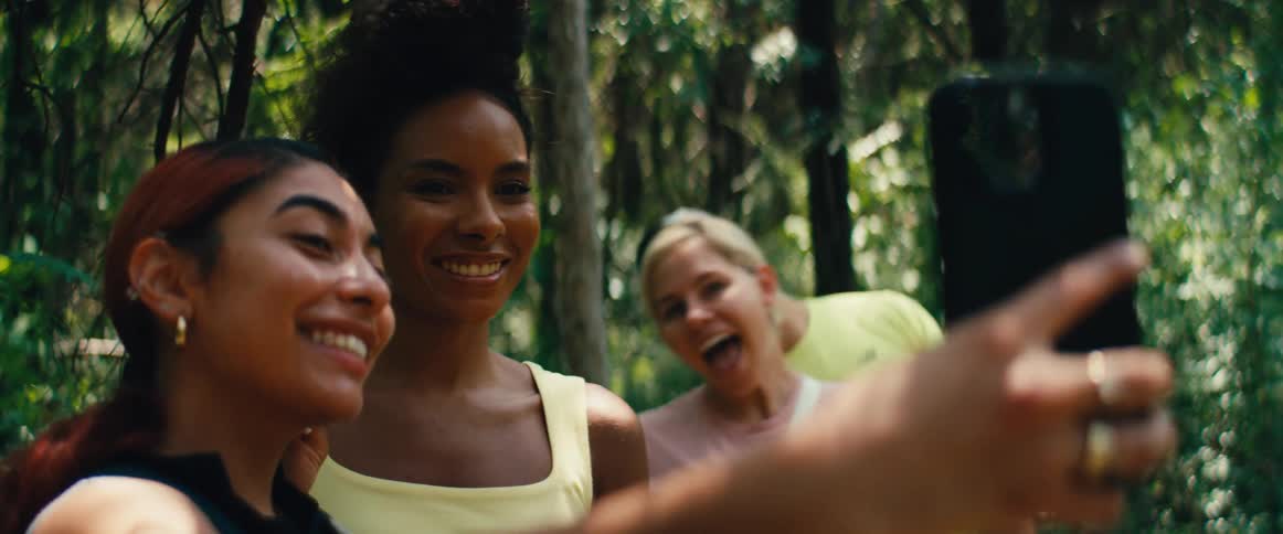A diverse group of friends laugh and smile while taking a fun selfie together in a sunny forest