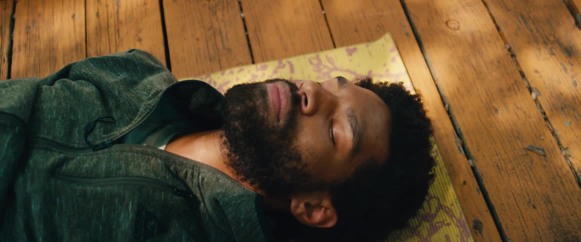 A tranquil man takes a moment to rest and meditate on a yoga mat placed on a rustic wooden floor