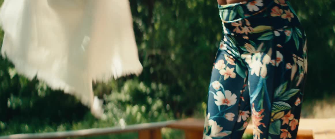 In slow motion, a woman gently places a blanket over a man meditating in a peaceful outdoor yoga class