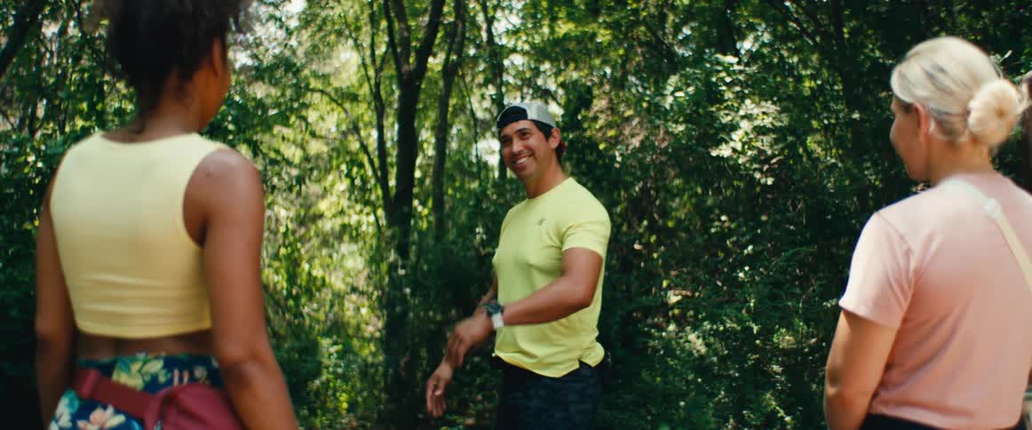 A male guide talks to a group of women before leading them on a hike through a lush, green forest