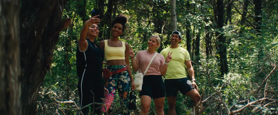 A diverse group of friends pauses during a hike in the woods to take a happy selfie together
