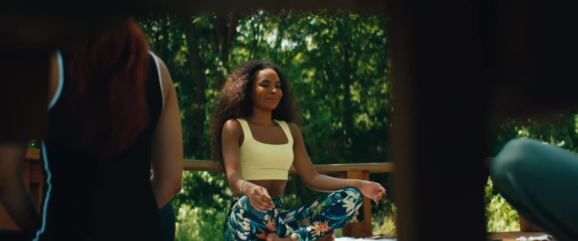 A beautiful woman with curly hair practices yoga and meditation during an outdoor class on a wooden porch