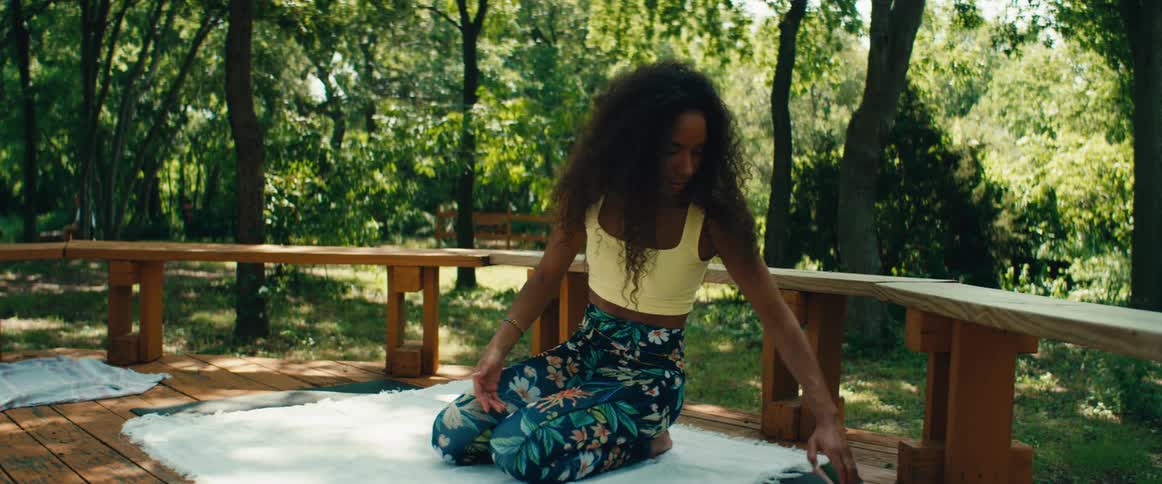 A smiling female fitness influencer sets up her phone and begins to lead a yoga class on a beautiful outdoor deck