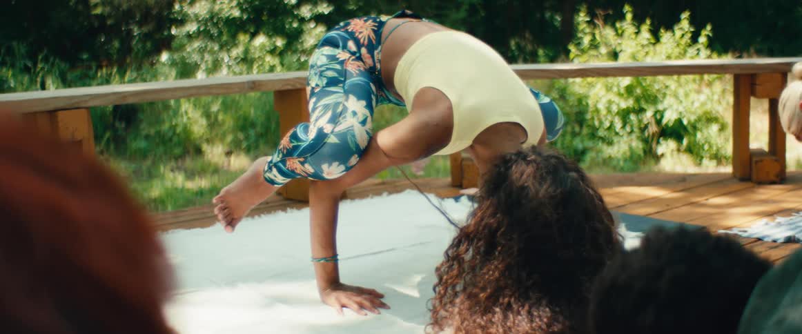 An athletic woman with beautiful curly hair gracefully transitions out of a challenging yoga pose in slow motion on an outdoor deck