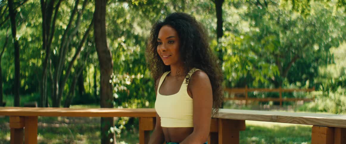 A focused African American woman with curly hair leads a mindfulness meditation session while sitting on a bench in a serene park