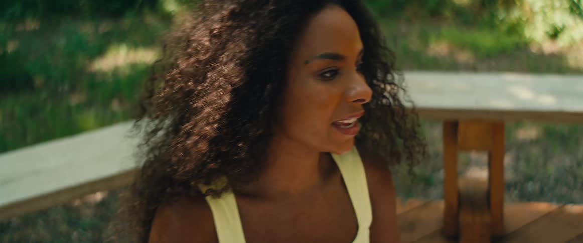 A beautiful woman with curly hair talks and gestures expressively while sitting outdoors in slow motion