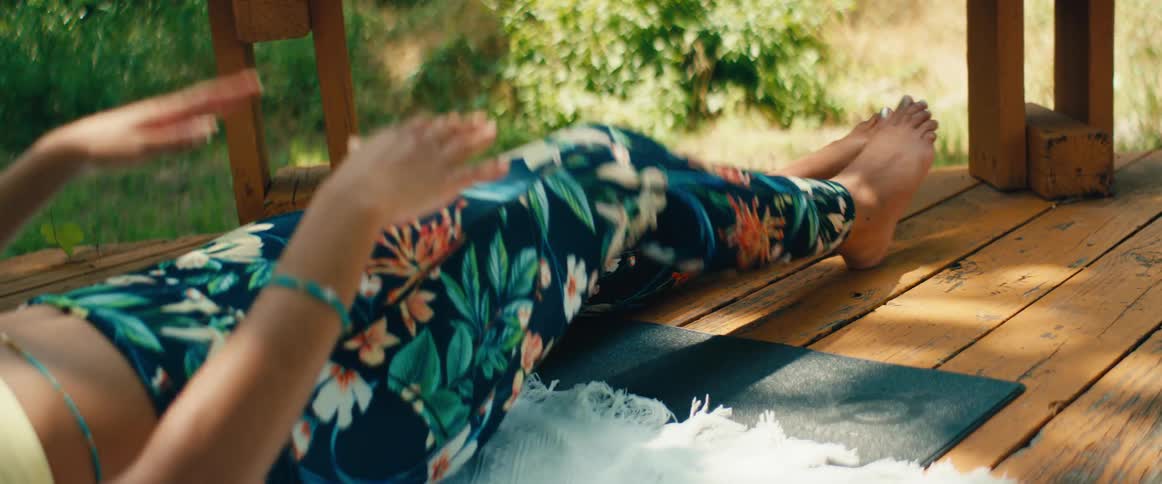 A serene woman with curly hair mindfully performs gentle yoga stretches in slow motion on an outdoor porch