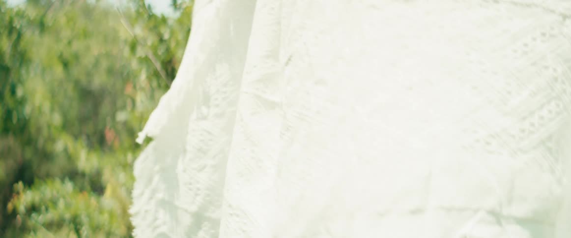 Dreamy close-up of a white textured blanket swaying in the wind on a clothesline in a sunlit garden
