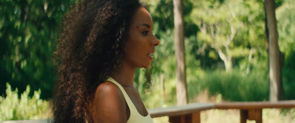 A beautiful yoga instructor with curly hair guides a meditation class outdoors, with the camera tilting down from her face to her hands