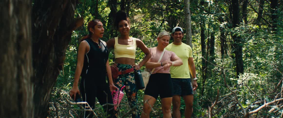 A diverse group of friends hiking through a sunlit forest stop to pose for a happy selfie together