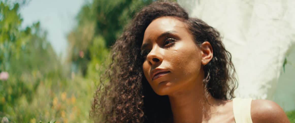 A beautiful woman with lush curly hair enjoys a serene moment, basking in the warm sunlight of a beautiful garden