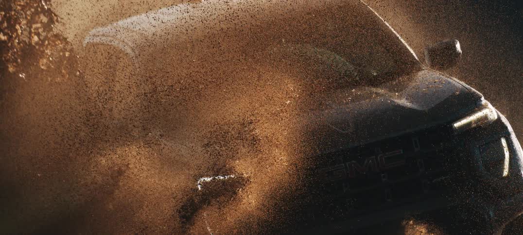 An extreme close-up of a black GMC truck splashing through thick mud in dramatic super slow motion