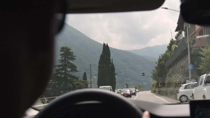 Over-the-shoulder slow-motion view from a driver's perspective on a scenic road trip through the lush green mountains of Italy