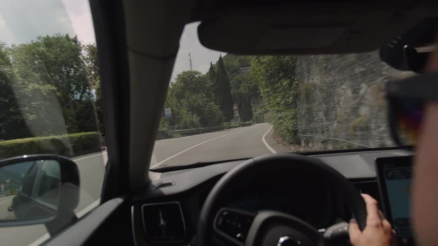 Over-the-shoulder view of a driver navigating a scenic, winding mountain road through a picturesque European village