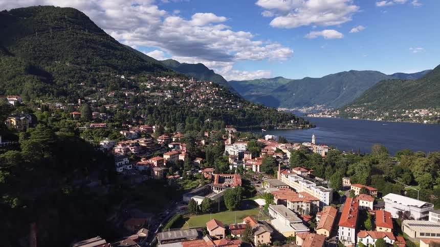 A stunning aerial view reveals the charming Italian town of Cernobbio on the picturesque shores of Lake Como, nestled among lush green mountains on a beautiful sunny day