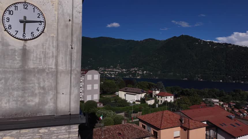 Aerial shot pushing past an old church bell tower to reveal a scenic Italian village nestled between mountains and a beautiful lake