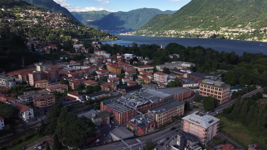Slowly receding aerial view of the city of Como, Italy, nestled on the shores of Lake Como with lush green mountains in the background
