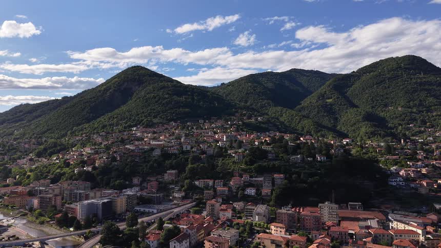 An idyllic Italian town is nestled at the base of lush green mountains on a beautiful sunny day