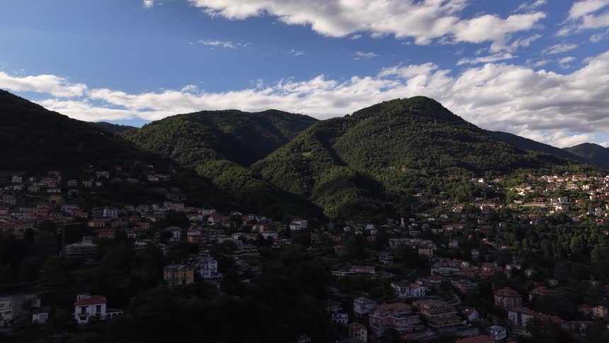 A stunning aerial view shows a picturesque village sprawling across the lush, green foothills of a mountain range