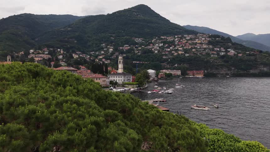 A slow aerial dolly shot reveals the picturesque town and marina on the shores of Lake Como, Italy, nestled against lush green mountains