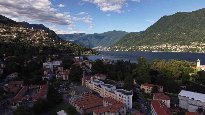 A stunning aerial view of a picturesque Italian town on the shores of Lake Como, surrounded by lush green mountains under a blue sky