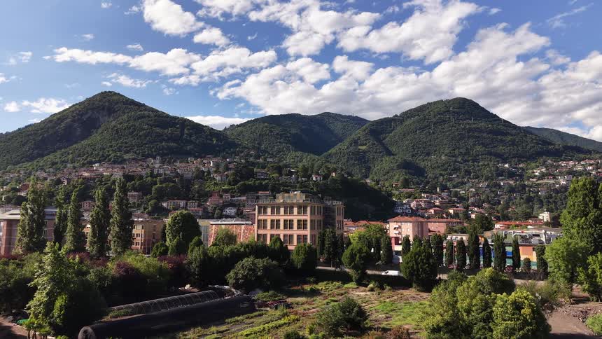Slow aerial pullback reveals an idyllic European town nestled in a valley surrounded by lush green mountains