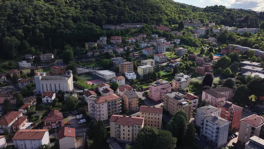 An aerial pullback reveals a quaint hillside town in Italy nestled against a dense green forest on a sunny day
