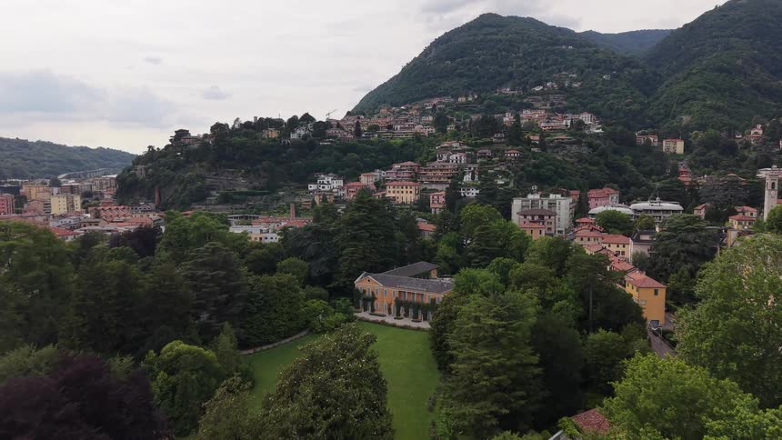 An aerial view reveals the stunning Villa Olmo nestled in its lush green park, with the charming city of Como, Italy spreading up the mountainside