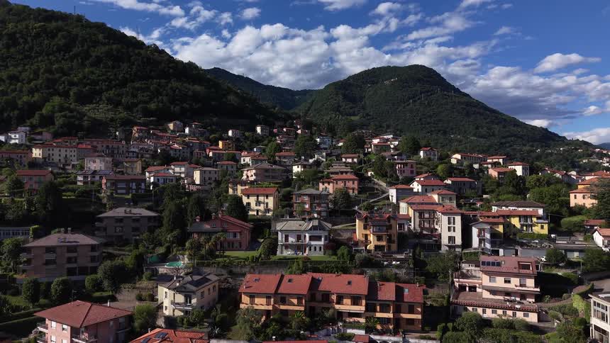 Aerial view slowly pulls back from a picturesque village nestled in the green mountains of Italy on a sunny day