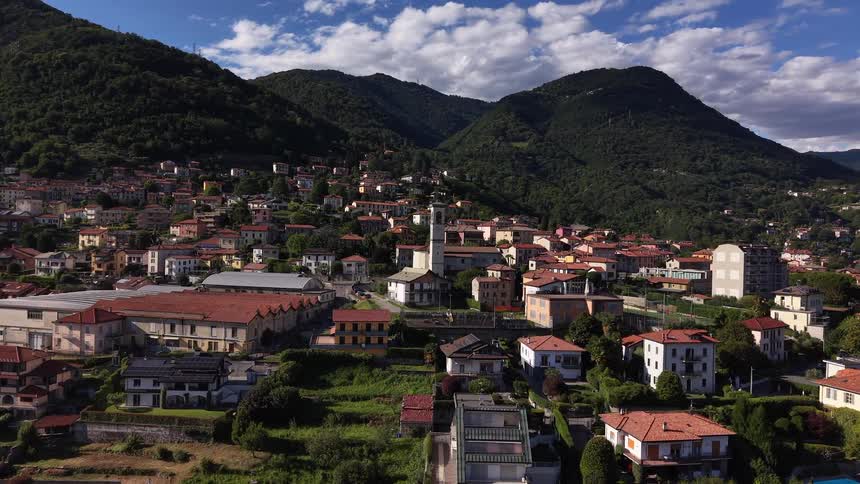 Sweeping aerial footage reveals a picturesque Italian village nestled at the base of lush green mountains