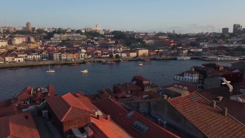 A stunning aerial view flies over the red rooftops of Porto's historic Ribeira district, revealing the Douro River with boats at sunrise