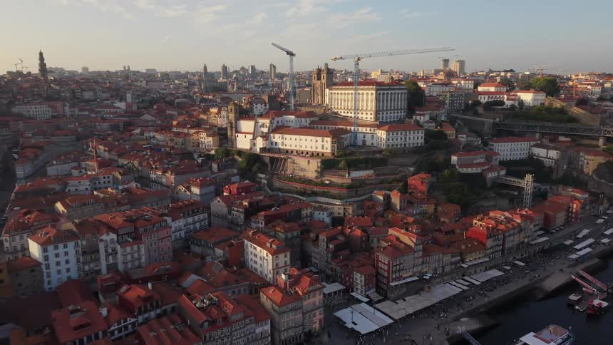 Stunning aerial view slowly pulling back over the historic red-roofed buildings of Porto, Portugal, along the Douro River at golden hour
