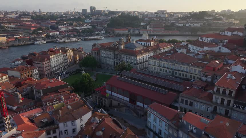 An aerial view pulls back over the historic red-roofed city of Porto, Portugal, revealing the Douro River at sunset