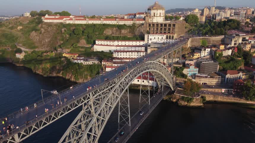 Stunning aerial pull-back view reveals the magnificent Dom Luís I Bridge over the Douro River in Porto, Portugal, bustling with pedestrians at sunset