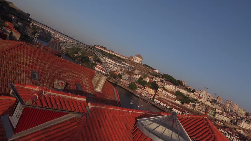 An aerial view rises over the terracotta rooftops of Porto, Portugal, revealing the scenic Douro River and the iconic Dom Luís I Bridge at golden hour