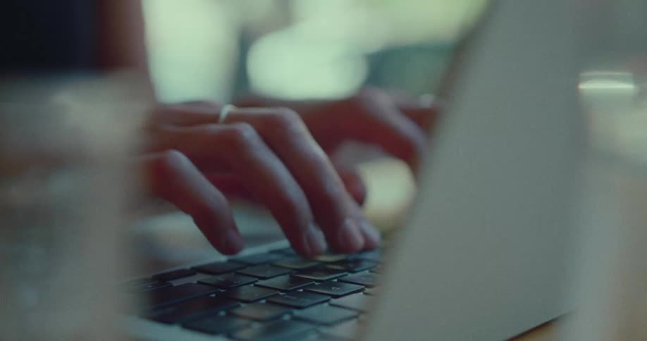 An artistic close-up shot of a person's hands typing on a laptop computer keyboard