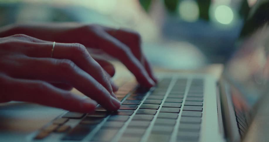 A close-up shot of a person's hands typing on a laptop keyboard in a softly lit, cozy environment