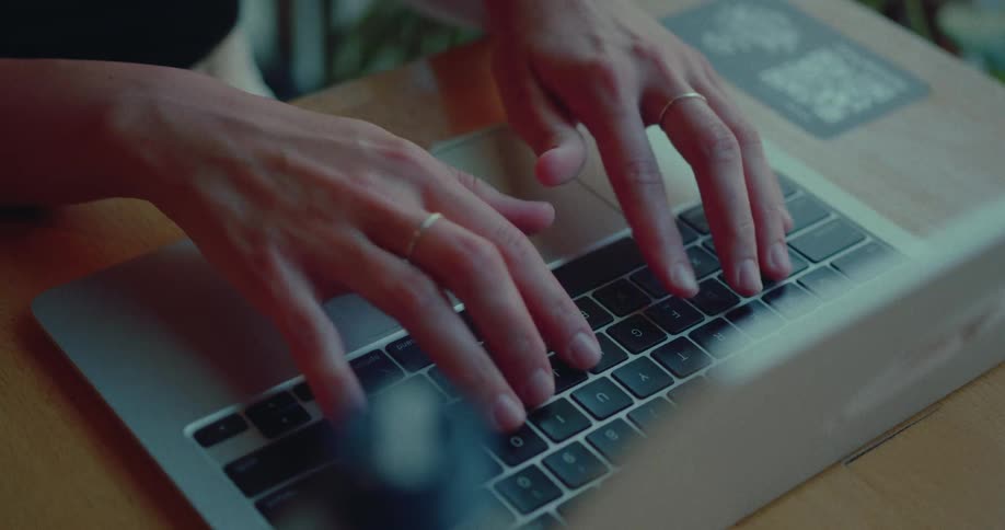 Fingers with delicate rings swiftly type on a laptop, focused on their work in a close-up view
