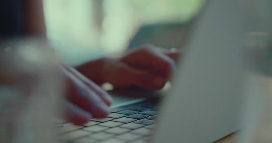 A dreamy, soft-focus close-up shows a person's hands typing on a laptop keyboard