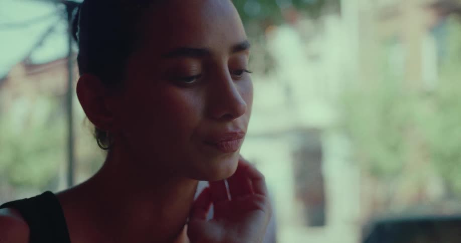 A pensive young woman with her hair in a bun sits alone at a cafe, lost in her thoughts