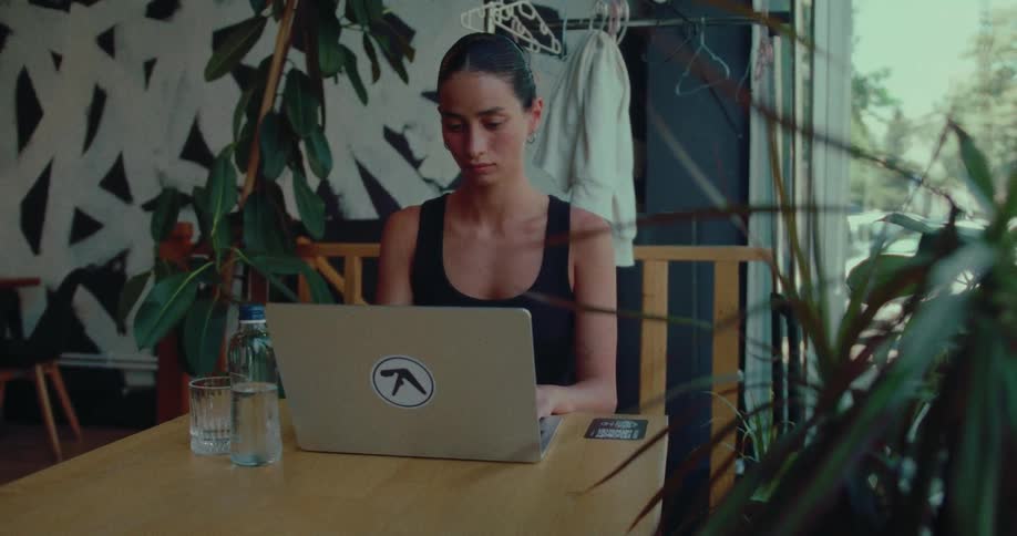 A young woman opens her laptop and begins working at a table in a stylish, modern cafe