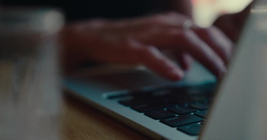 A close-up, slow-motion shot of a person's hands typing on a laptop computer keyboard