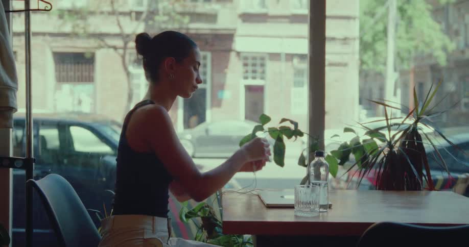 A focused young woman in a cafe closes her laptop and pauses to watch the city life outside the window