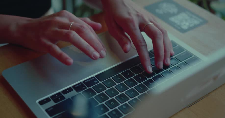 A close-up shot of a woman's hands typing and using the trackpad on a modern laptop on a wooden desk